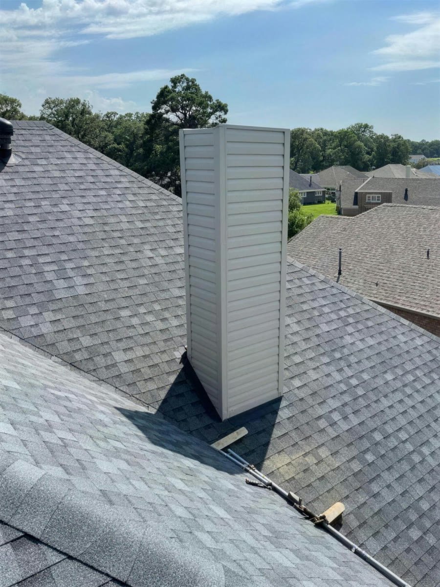 New sided chimney chase rising from a gray shingle roof under a blue sky